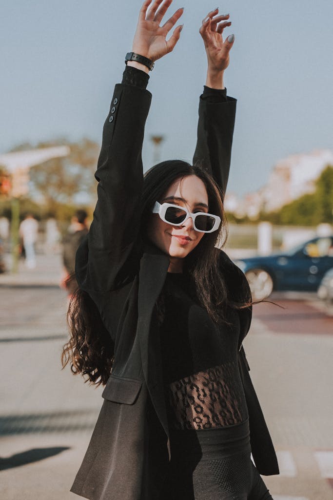 Confident young woman in black outfit with arms raised, enjoying a sunny day in Spain.